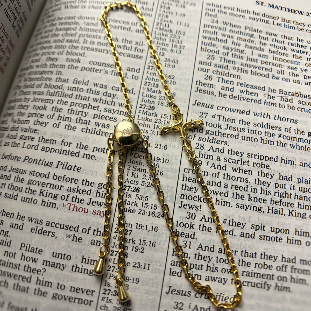 A gold-toned metal crucifix pendant with a hanging chain, displayed on an open Bible with printed text visible in the background.