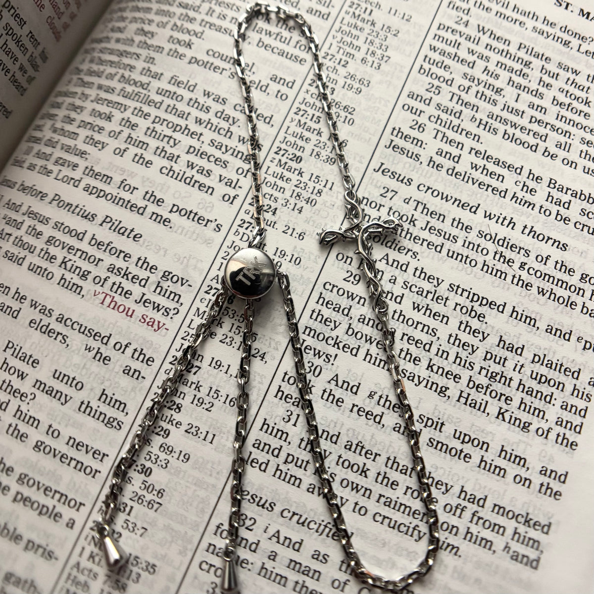 A silver-toned metal chain necklace with a small round pendant and a cross-shaped charm, laid out on an open book with printed text.