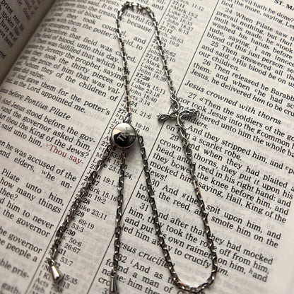 A silver-toned metal chain necklace with a small round pendant and a cross-shaped charm, laid out on an open book with printed text.