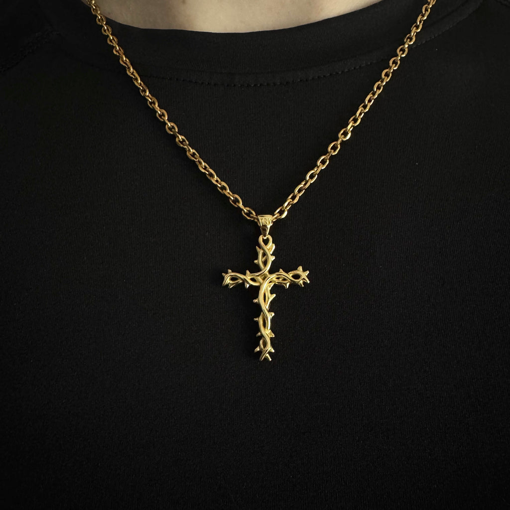 A gold cross pendant necklace with a thorny design, worn on a black shirt.