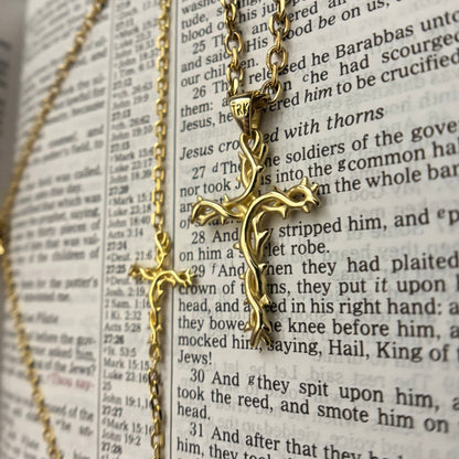 A gold-toned crucifix pendant necklace draped over an open Bible, with the chain looping along the left side of the frame.